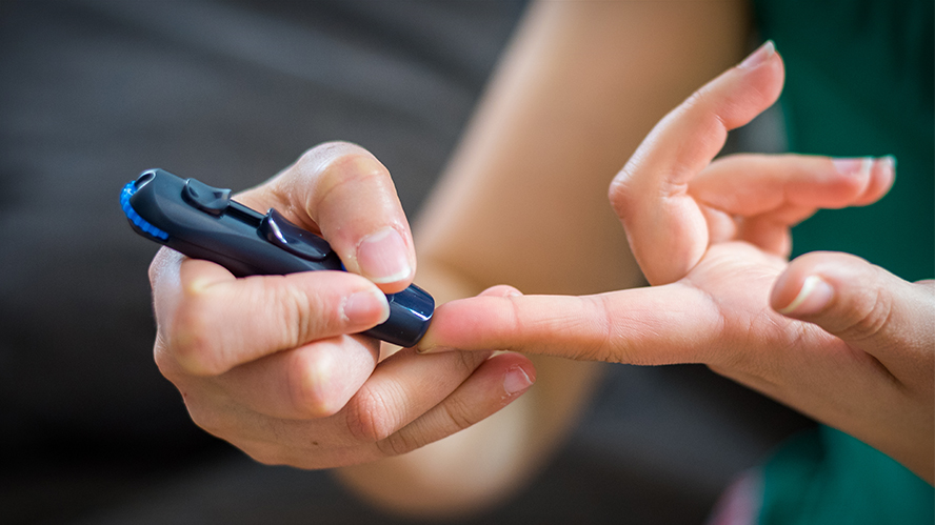 Person pricking finger with a diabetes glucose monitor.